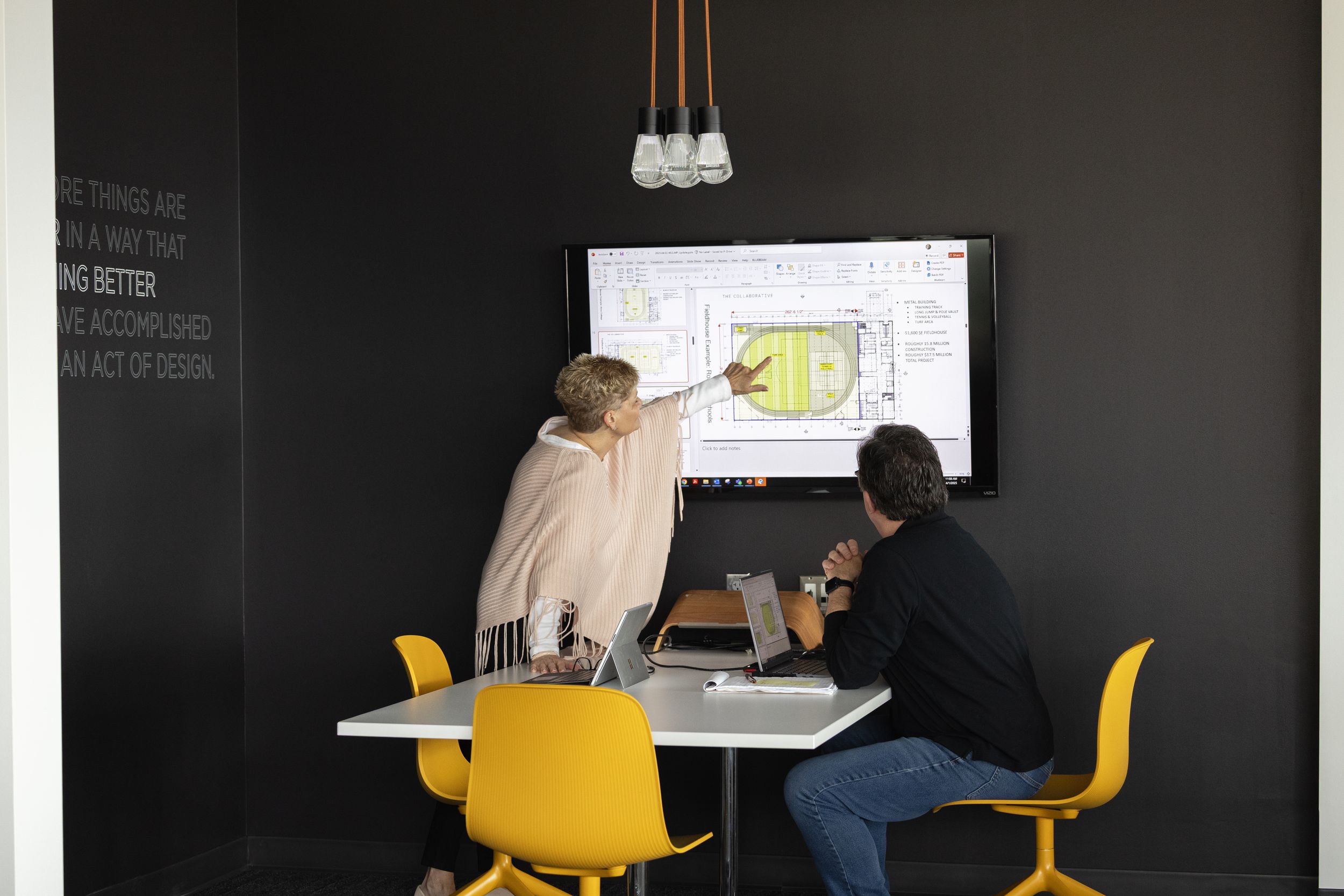 A modern workspace with black walls and yellow chairs features multiple desk setups for collaborative work.