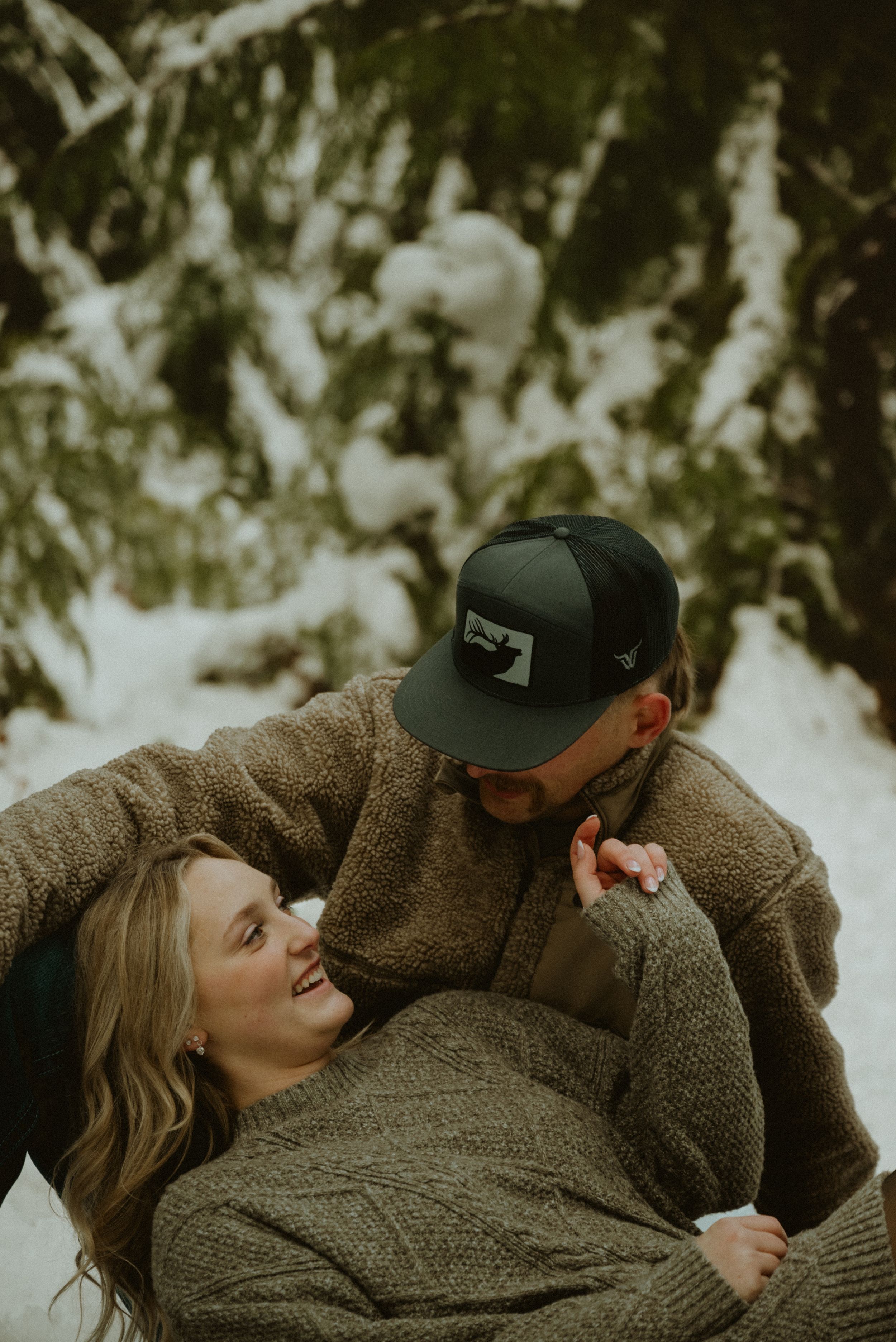 A romantic couple embraces while wearing cozy winter clothing in a snowy outdoor setting.
