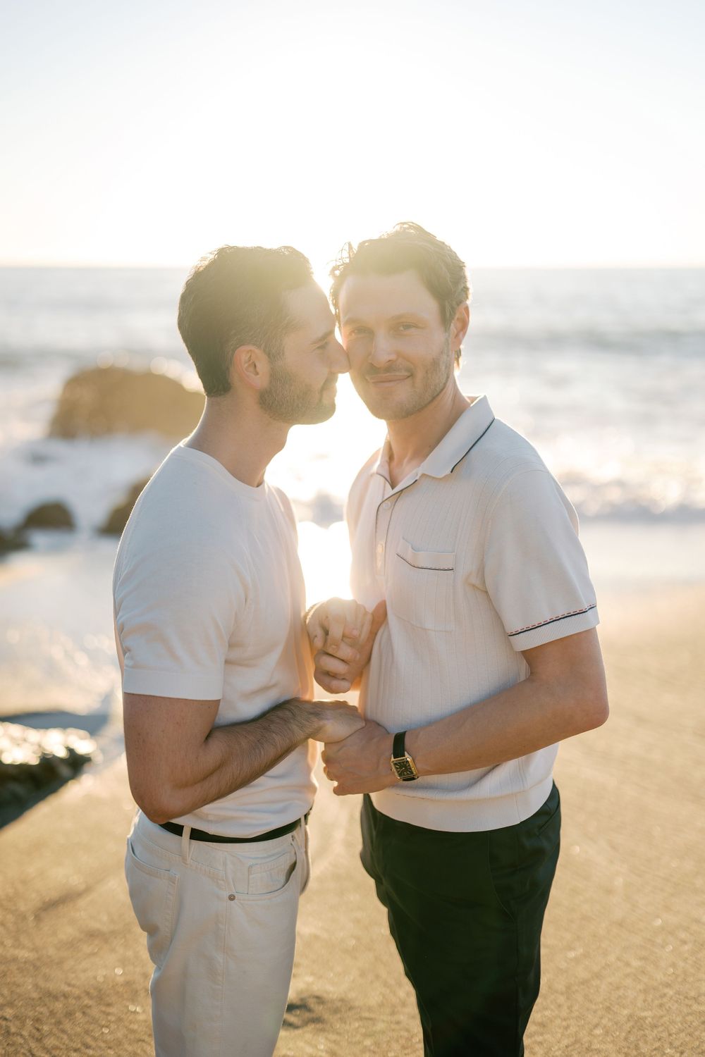 A couple shares an intimate moment together on a sunny beach at golden hour.