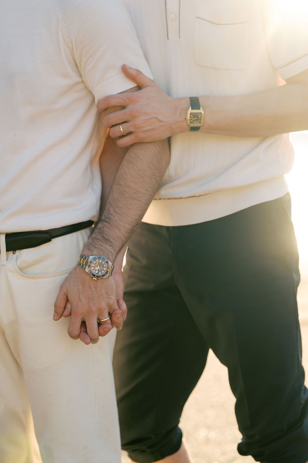Close-up sequence showing hands wearing rings and a watch against a white shirt and dark pants background.