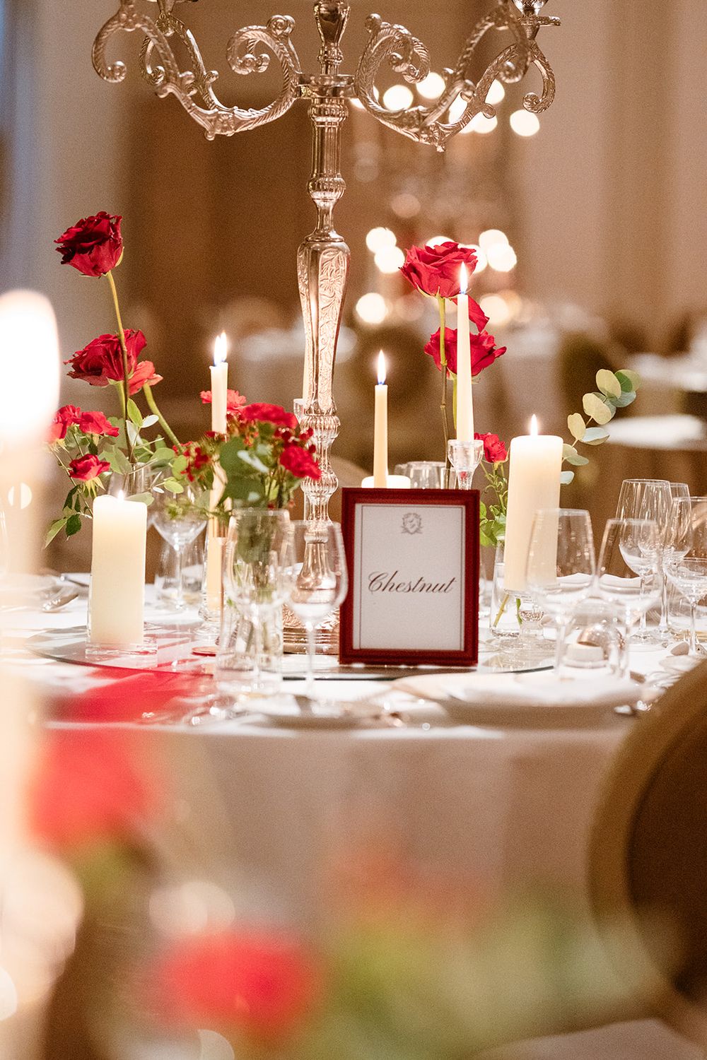 Elegant wedding reception table setting with white candles and red roses creating a romantic ambiance.