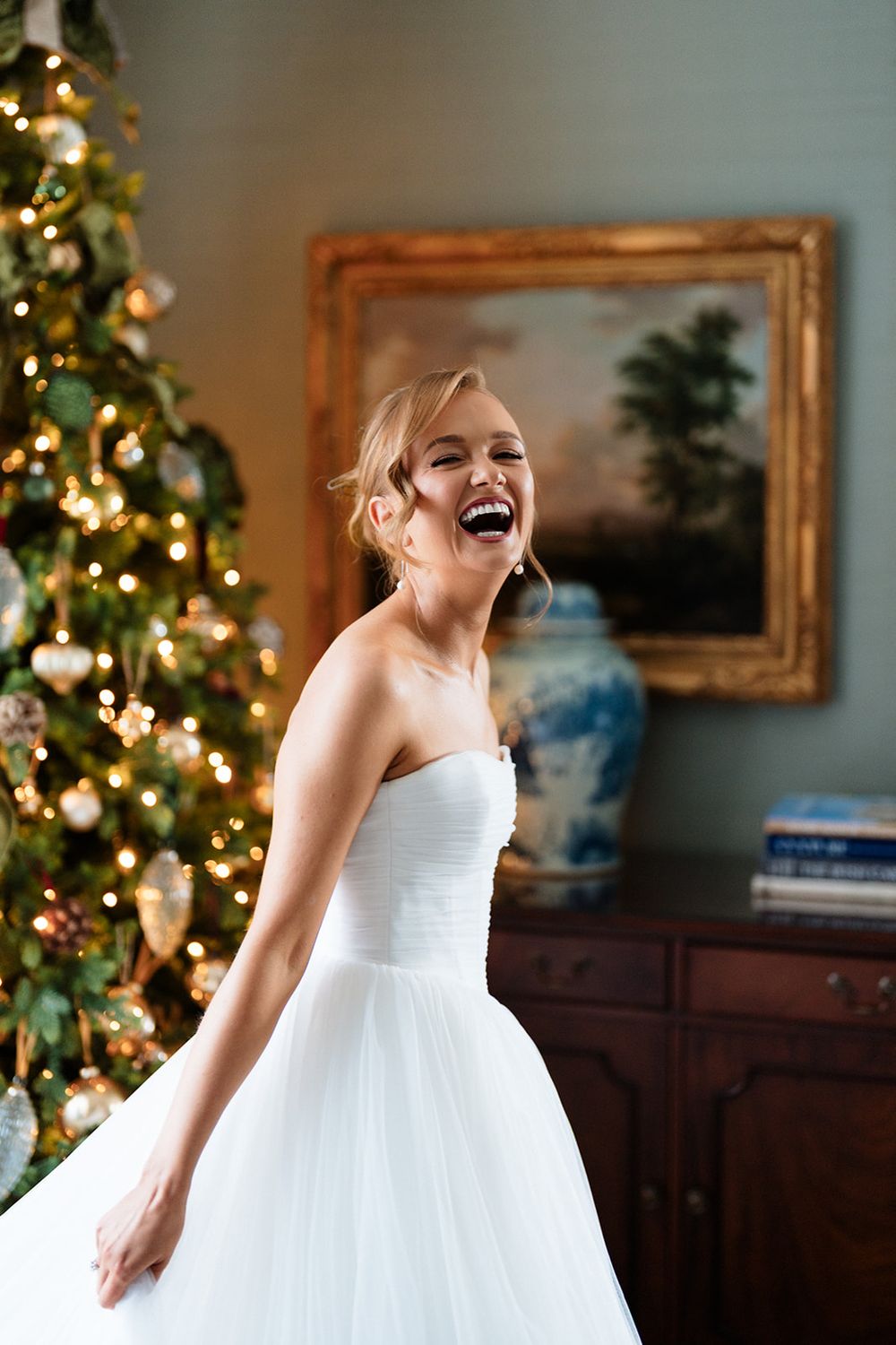 A joyful figure in a white dress laughs against a backdrop of twinkling Christmas trees and framed artwork.
