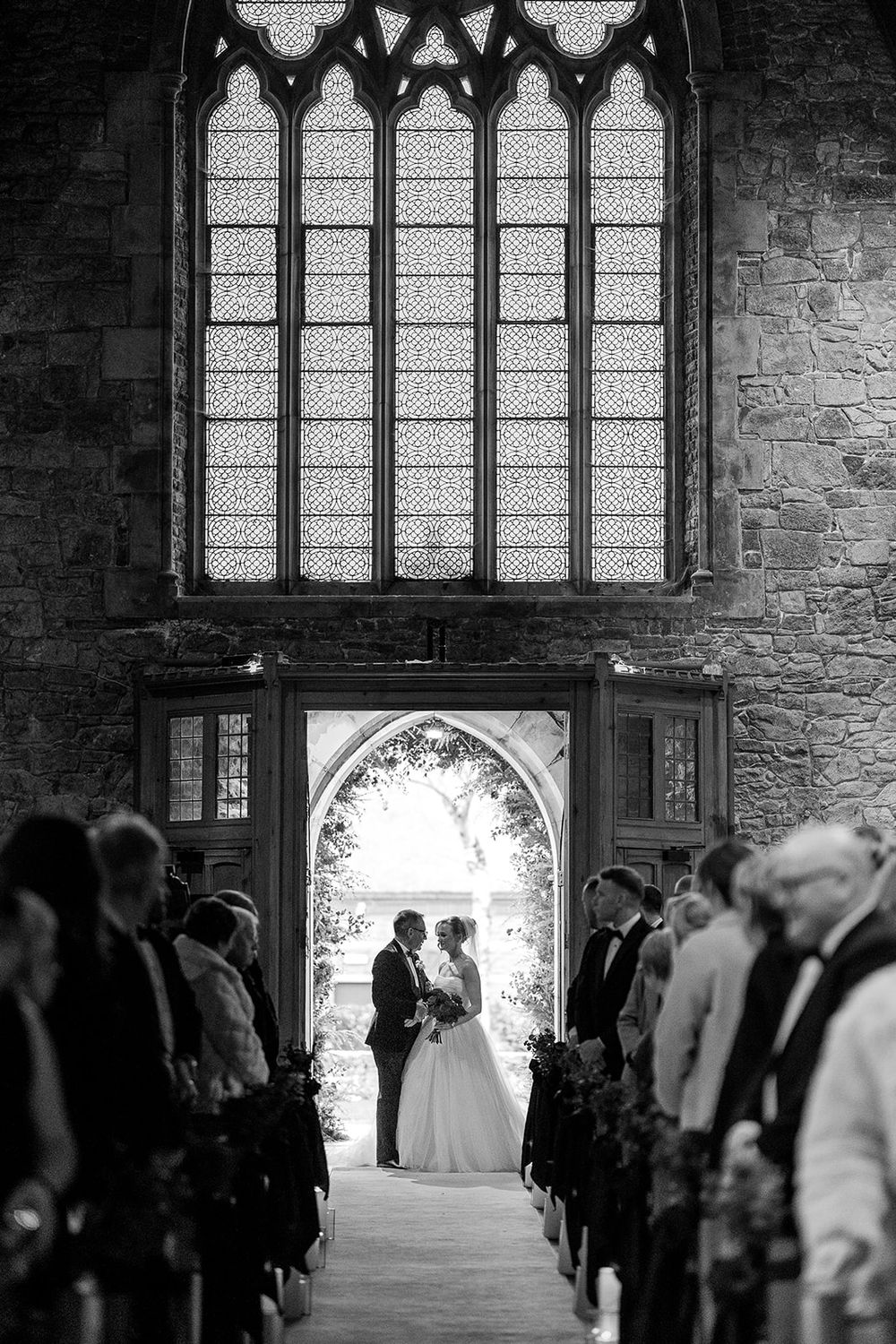 A silhouetted wedding ceremony inside a gothic church with ornate stained glass windows and stone walls - Adare Manor Weddings by Sarah Kate