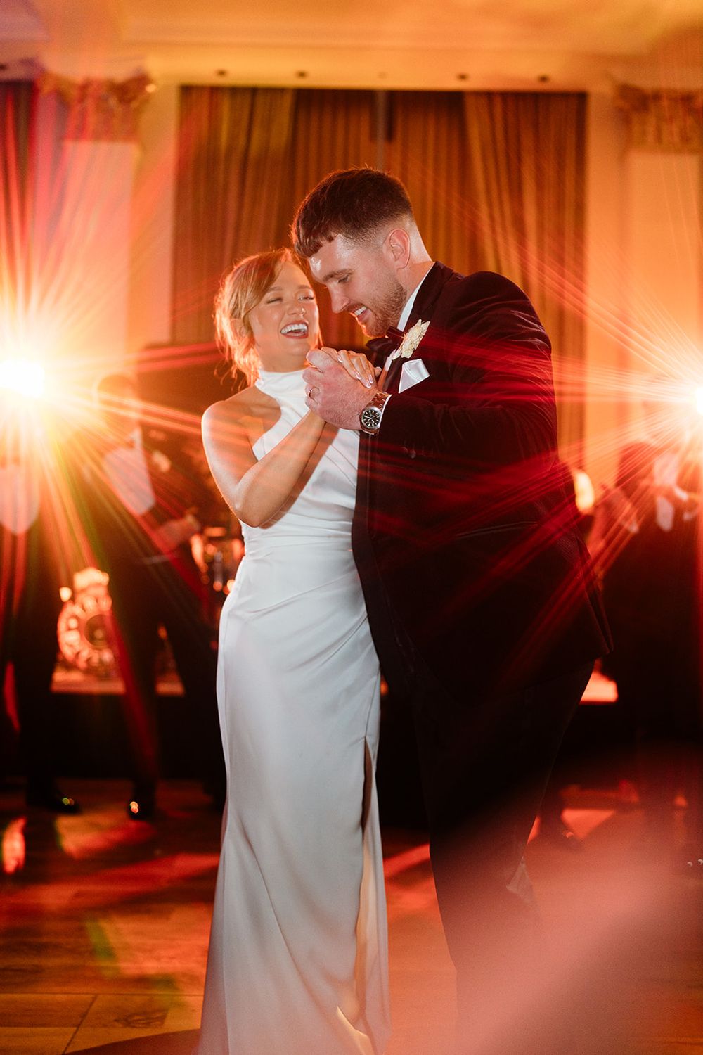 A couple shares a romantic dance moment in warm amber lighting at their wedding reception.