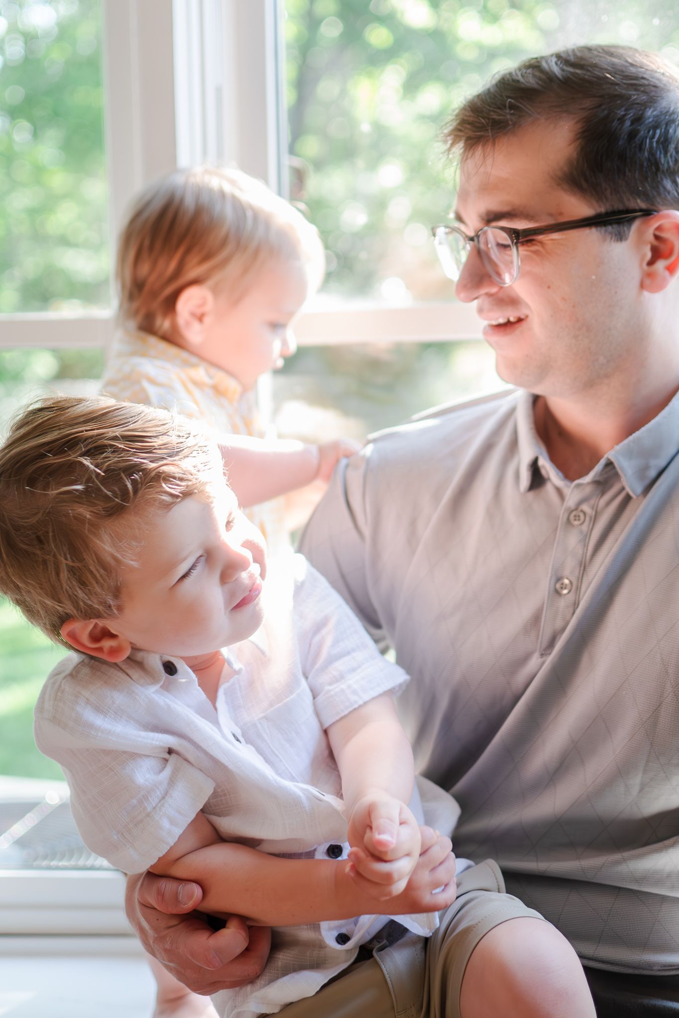 A sequence of five candid photos showing playful interaction between a parent and child by a window.