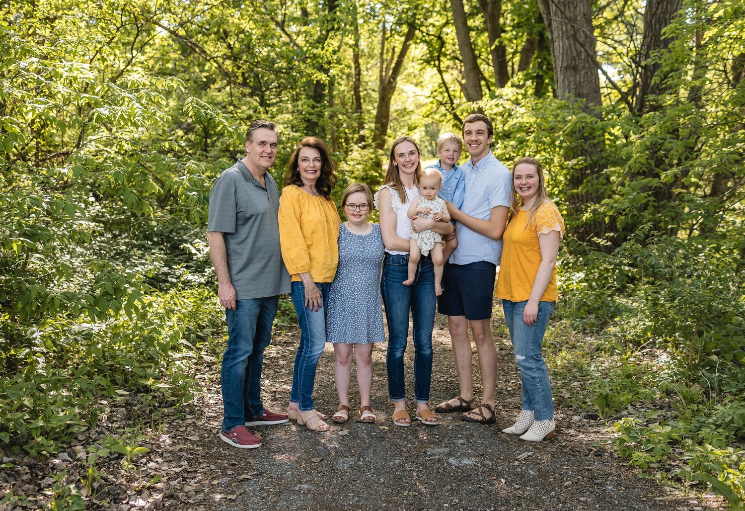 A group of people in coordinated blue and yellow outfits pose together in a lush wooded outdoor setting.
