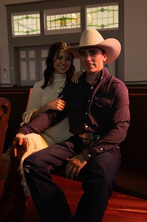 A young couple in Western attire sits on a church pew, the man wearing a cowboy hat and woman in a turtleneck sweater.