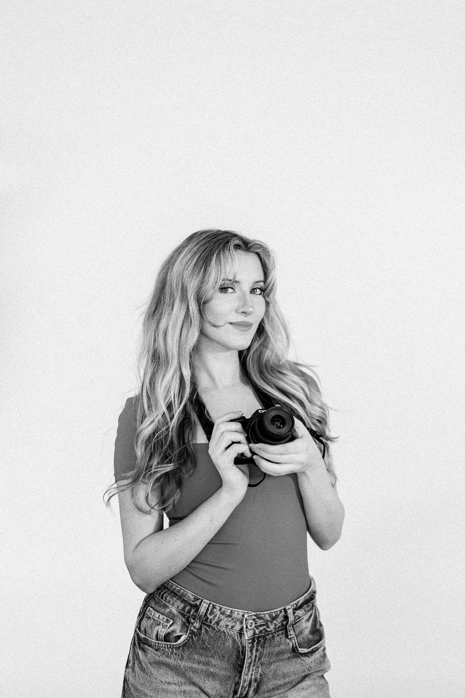 A photographer in casual attire poses with a camera in various positions against a white backdrop.