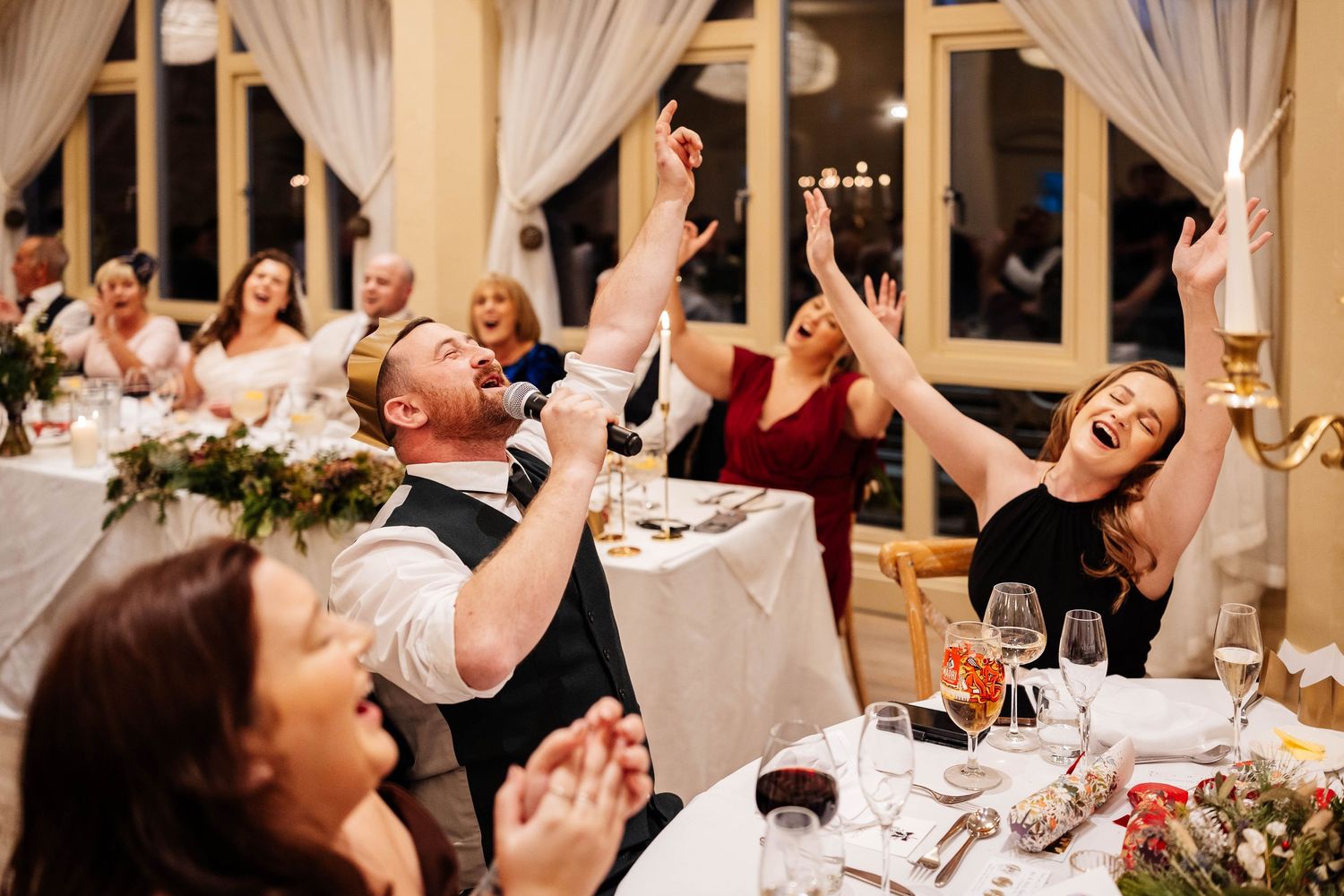 Candid wedding breakfast moment, of wedding guests singing at dancing at the table at Wennington Hall, hosted by Howard Wing
