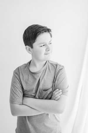 Black and white portrait of a young person in a gray t-shirt standing with arms crossed against a light background.