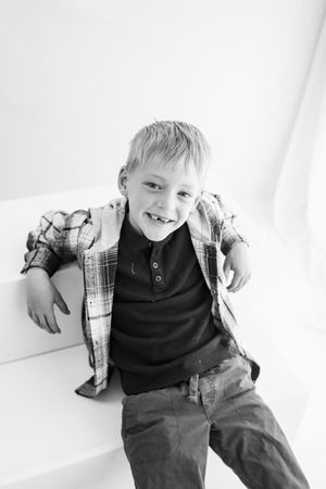 A smiling young boy with missing teeth wearing a plaid shirt poses playfully in a black and white portrait photo.