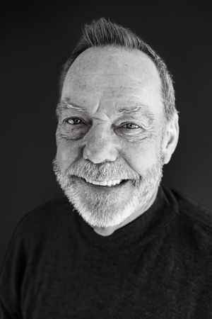 Black and white portrait of a smiling older man with a gray beard wearing a dark turtleneck sweater.
