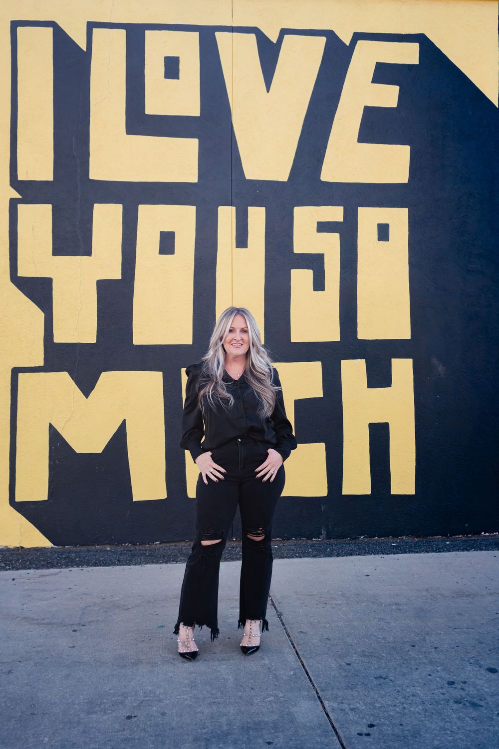 Four sequential photos showing a person in black clothing posing against a large black and white text mural on a wall.