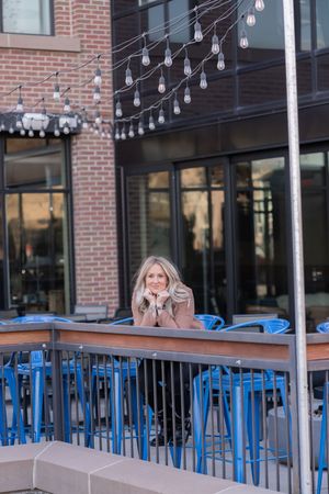 Outdoor restaurant patio with blue metal barstools and string lights at sunset against a brick building exterior.