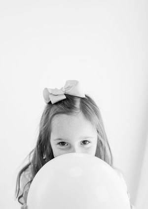 Black and white photo of a young girl with a bow in her hair, peeking over a large white balloon.