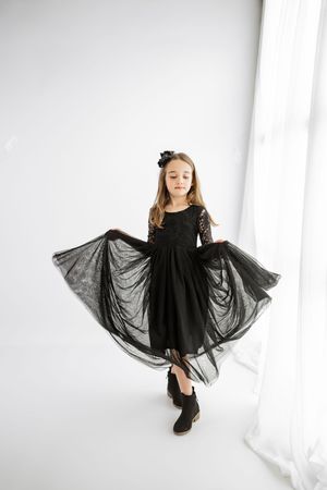 Young girl in black lace tulle dress twirling in white studio, wearing black shoes and floral headband.