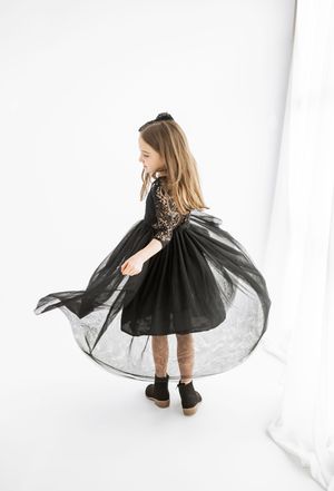 Young girl twirling in a black lace and tulle dress with long sleeves on a white background.