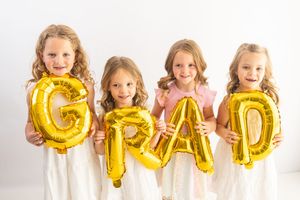 Four young girls holding gold foil GRAD balloons smiling against a white background.