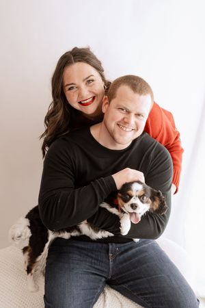 A couple poses together with their small black and white dog in a series of casual indoor portrait photos.