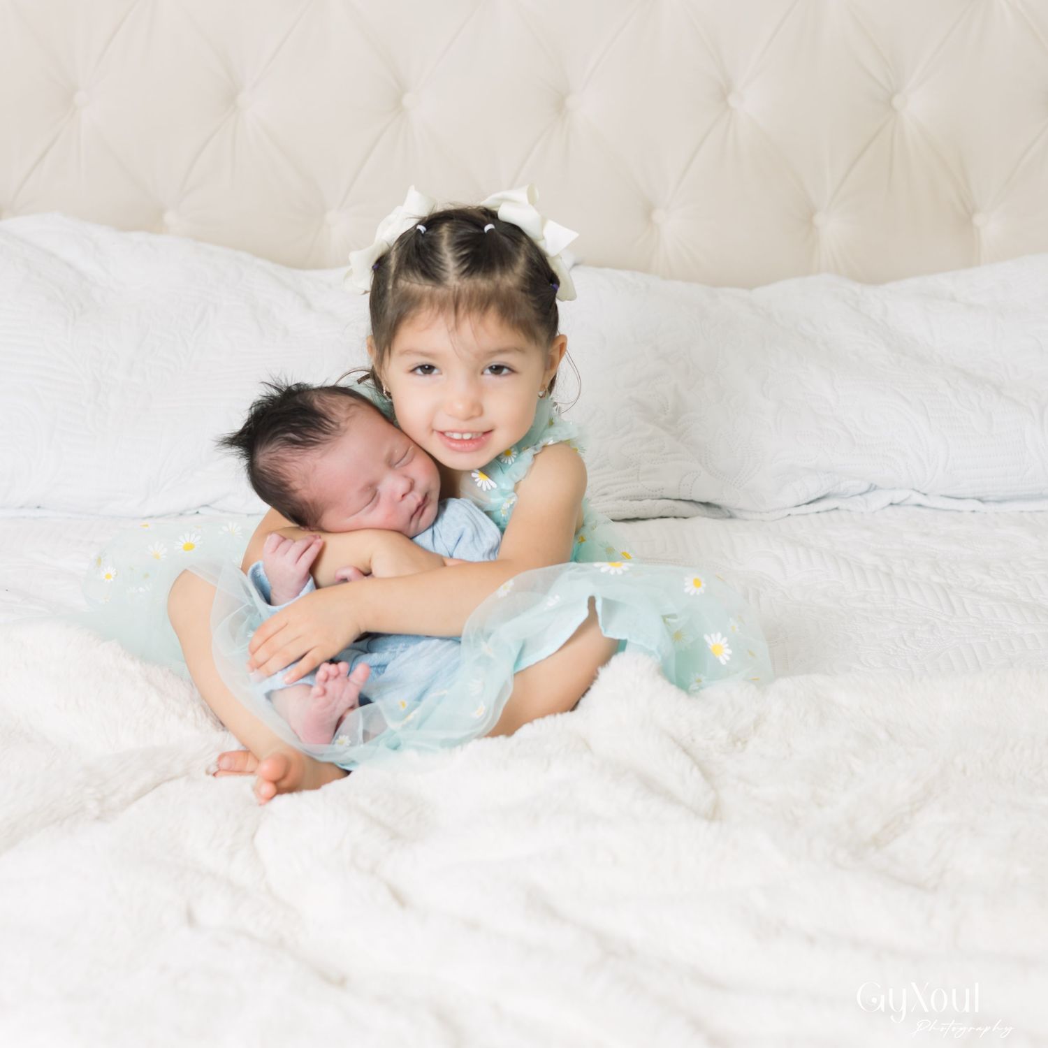 A child in a light blue dress lies on white bedding in a series of playful poses.
