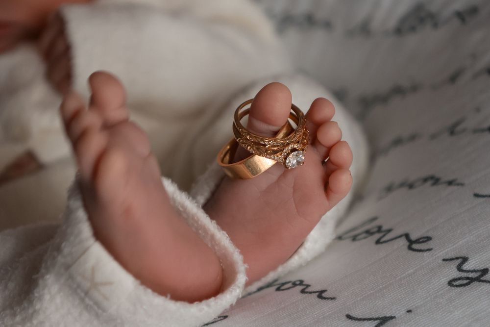 Close-up of tiny baby foot with gold ring resting on script-patterned fabric.