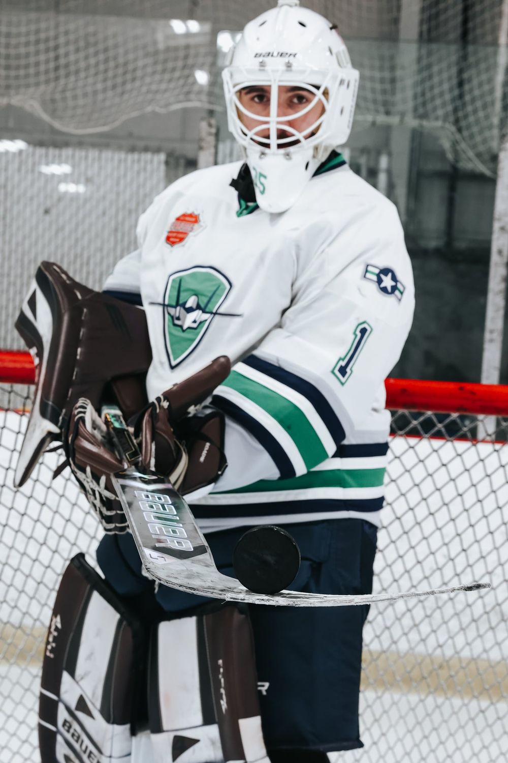 Hockey player in white and green jersey practicing shots at indoor rink.