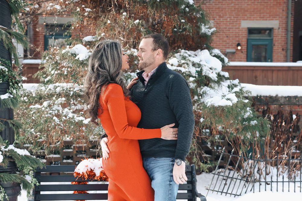 Romantic winter photoshoot with couple embracing in front of snow-covered scenery.