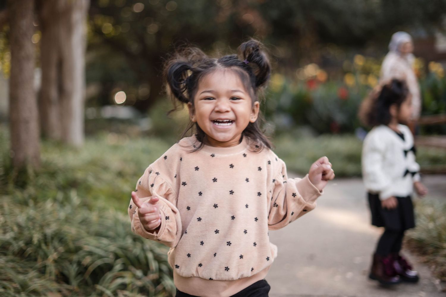 Joyful young girl in polka dot sweatshirt laughing and running in a park.