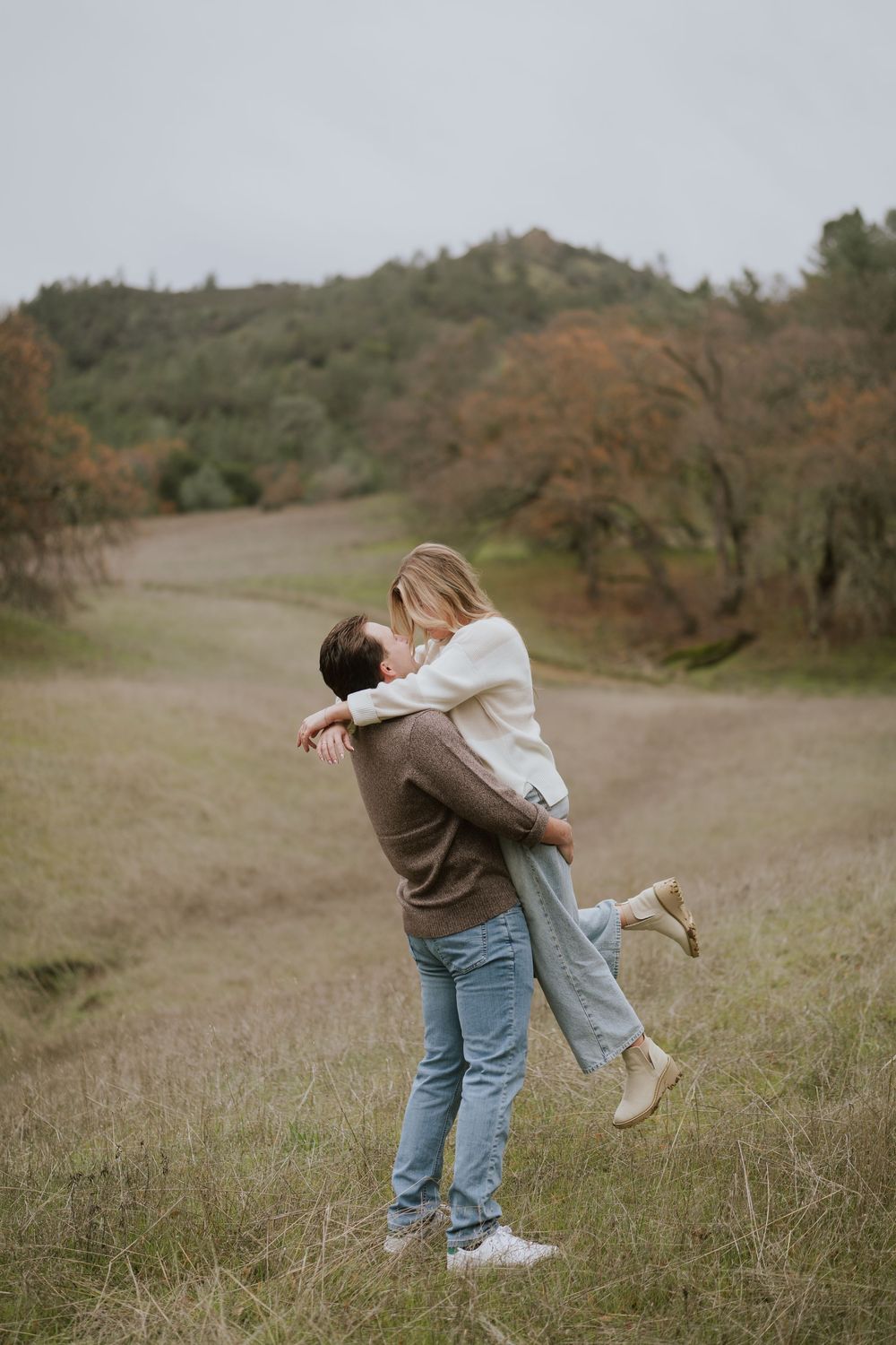 A couple embraces and spins together in a romantic moment on a grassy hillside during autumn.