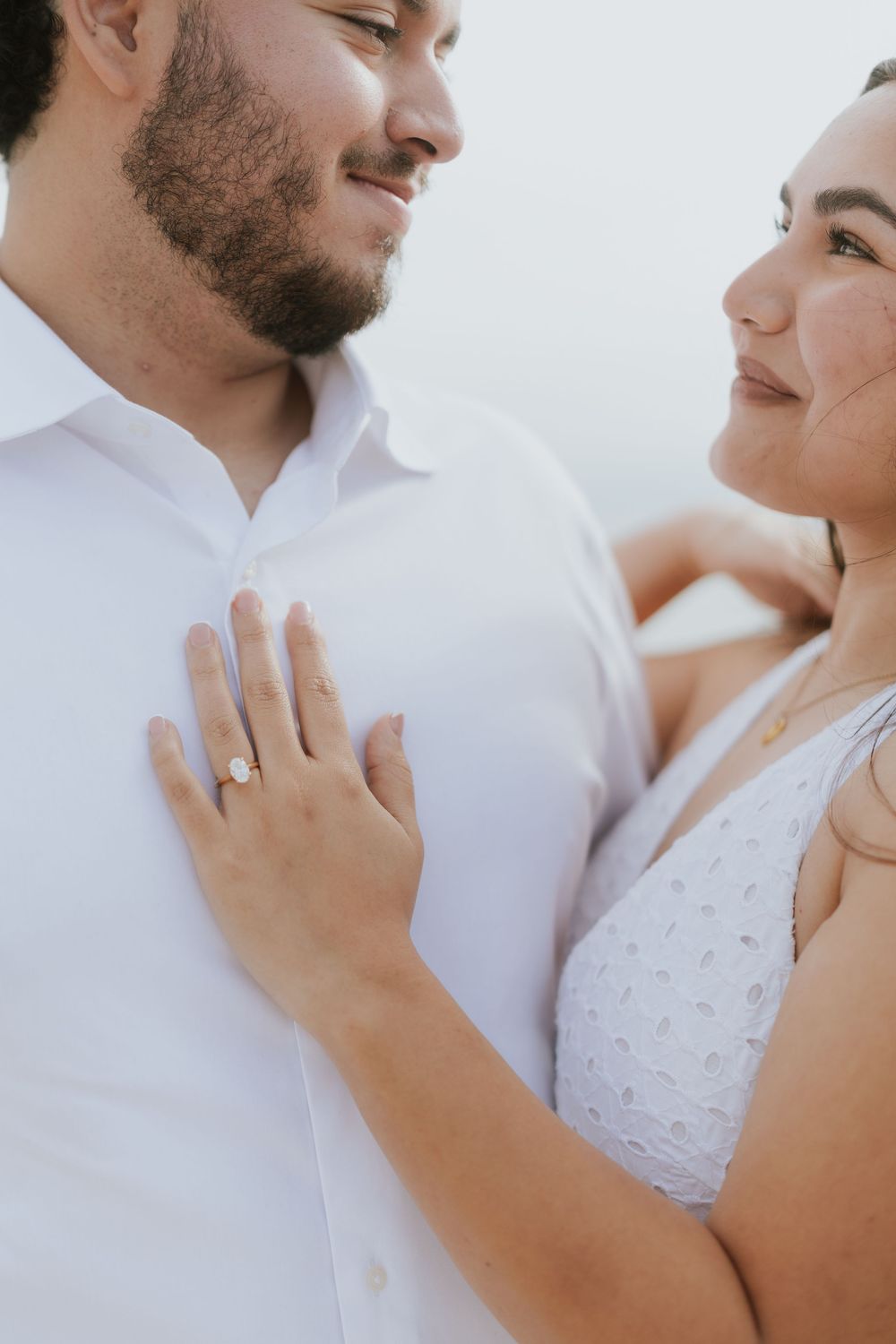 A romantic couple in white embraces tenderly during an engagement photoshoot showing their close connection.