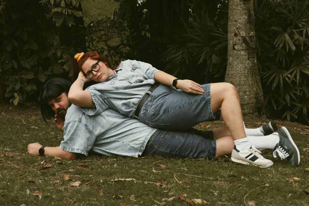 A person lies peacefully on grass in a park setting wearing casual attire and sneakers.