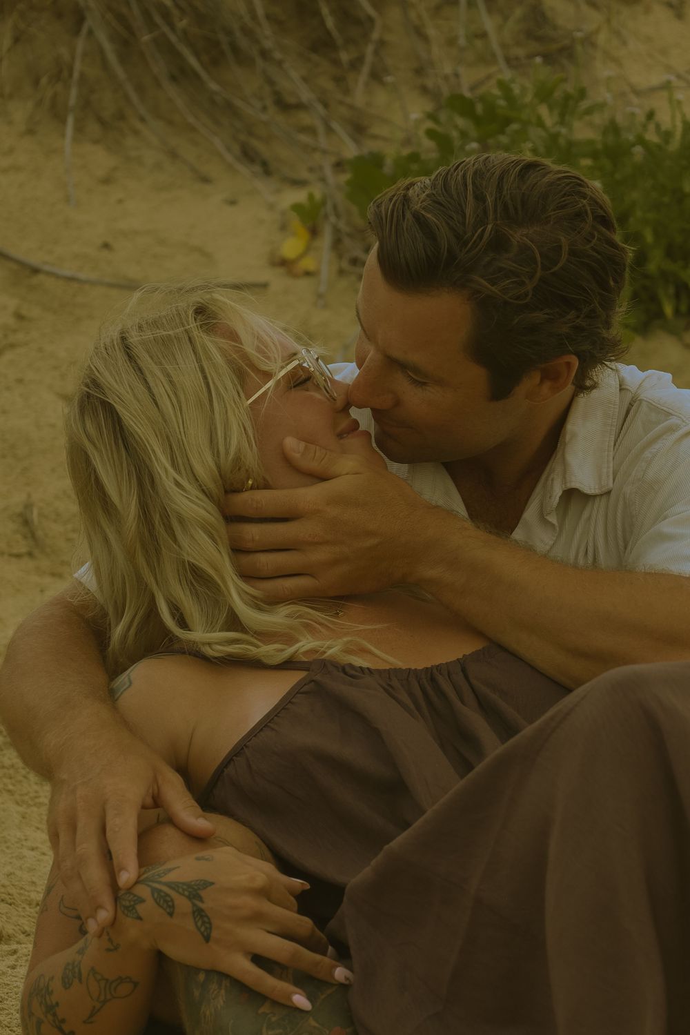 A romantic couple embraces tenderly on sandy ground during golden hour in a dreamy, intimate moment.