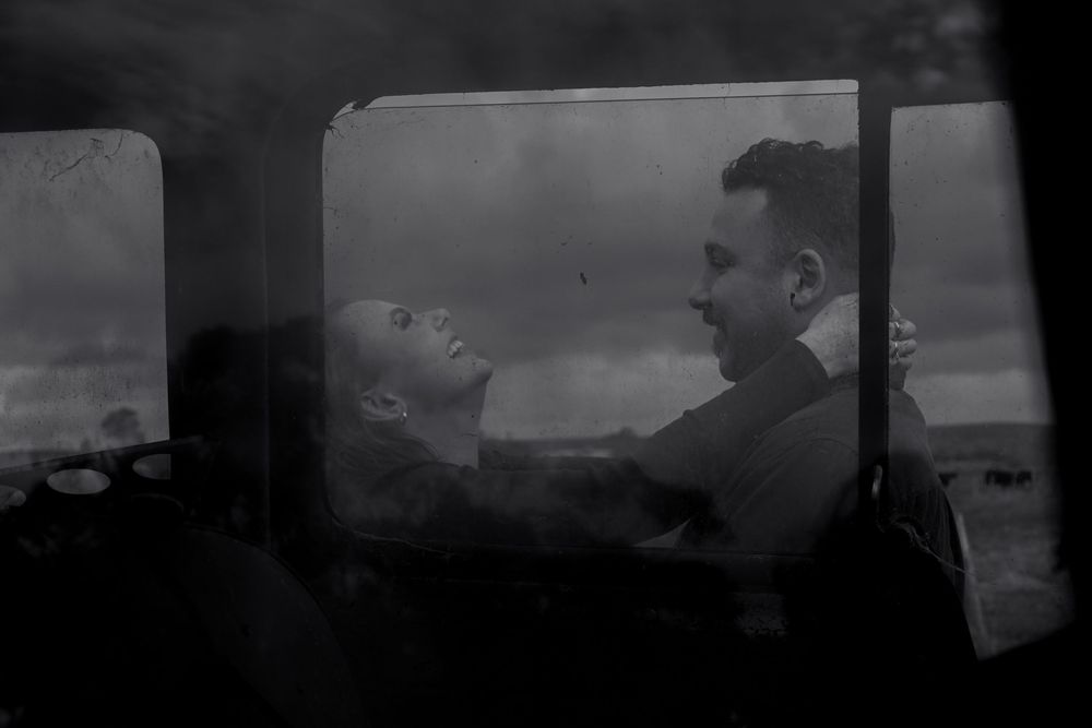 A black and white photograph showing two people in silhouette through a car window.