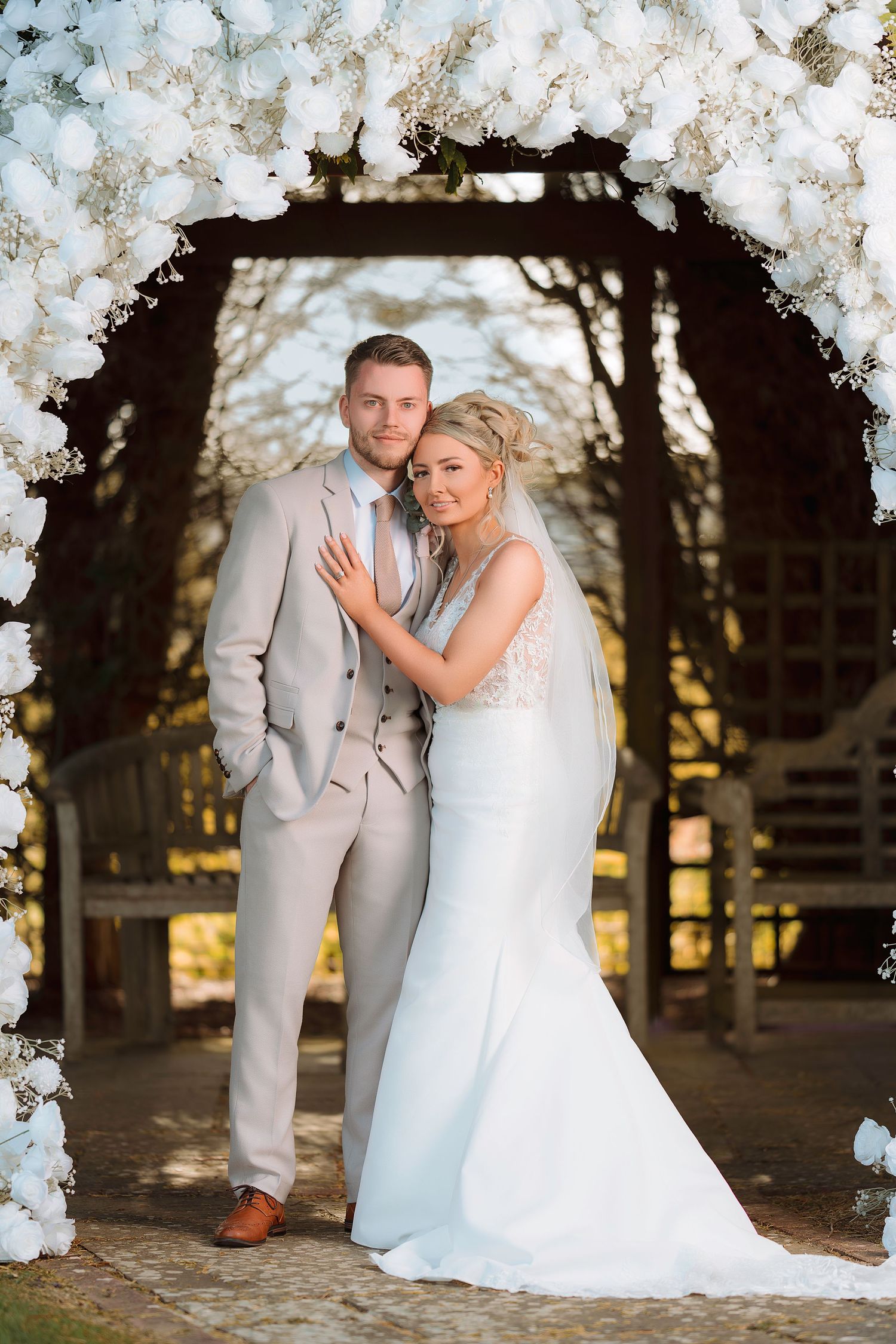 Romantic wedding couple poses under blooming cherry blossom trees during sunset at a rustic outdoor venue.