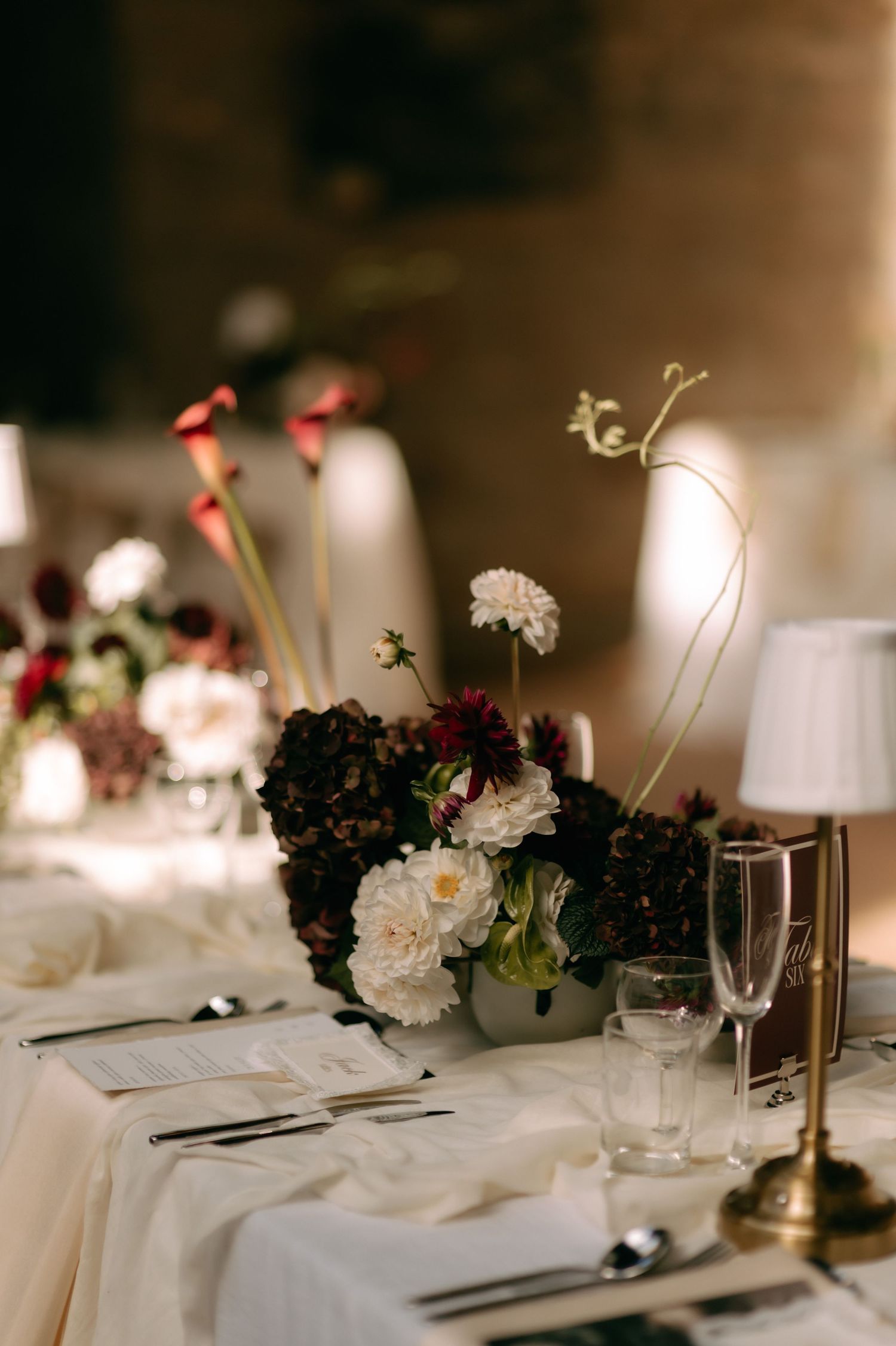 Elegant wedding reception table settings with white linens, burgundy floral centerpieces, and soft candlelight create a romantic ambiance.