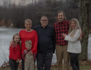 Family of six poses together outdoors by a lake on an overcast winter day wearing red and neutral colors.