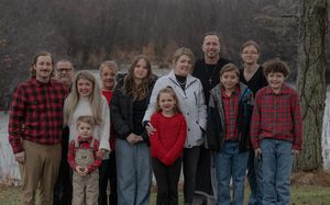 Large family group poses together outdoors wearing coordinated casual clothing by a lake.