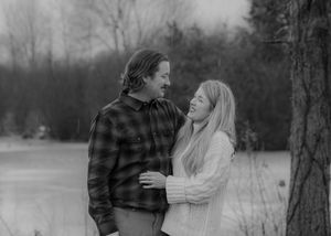 Couple in buffalo plaid and white sweater share intimate moment against winter landscape.