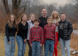 Group portrait of eight people in casual attire posed together outdoors on an autumn day.
