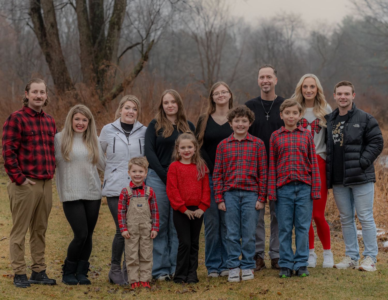 Large family group wearing coordinating red and casual outfits poses together outdoors in autumn setting.