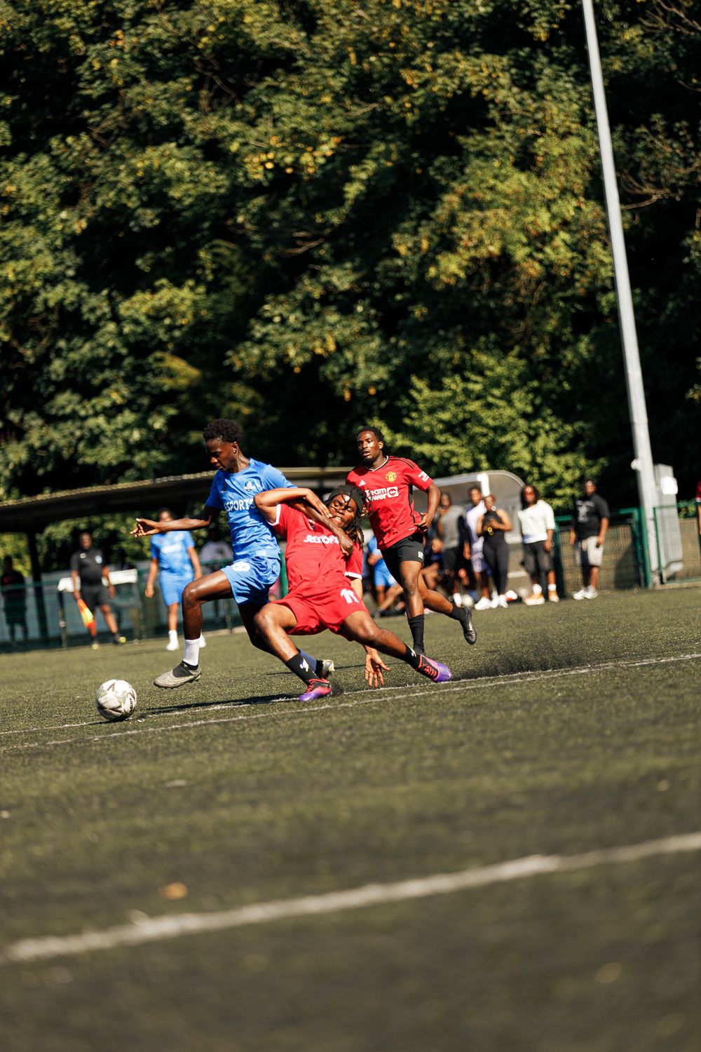 Soccer players in red and blue uniforms dive for the ball during an intense match on a grass field.