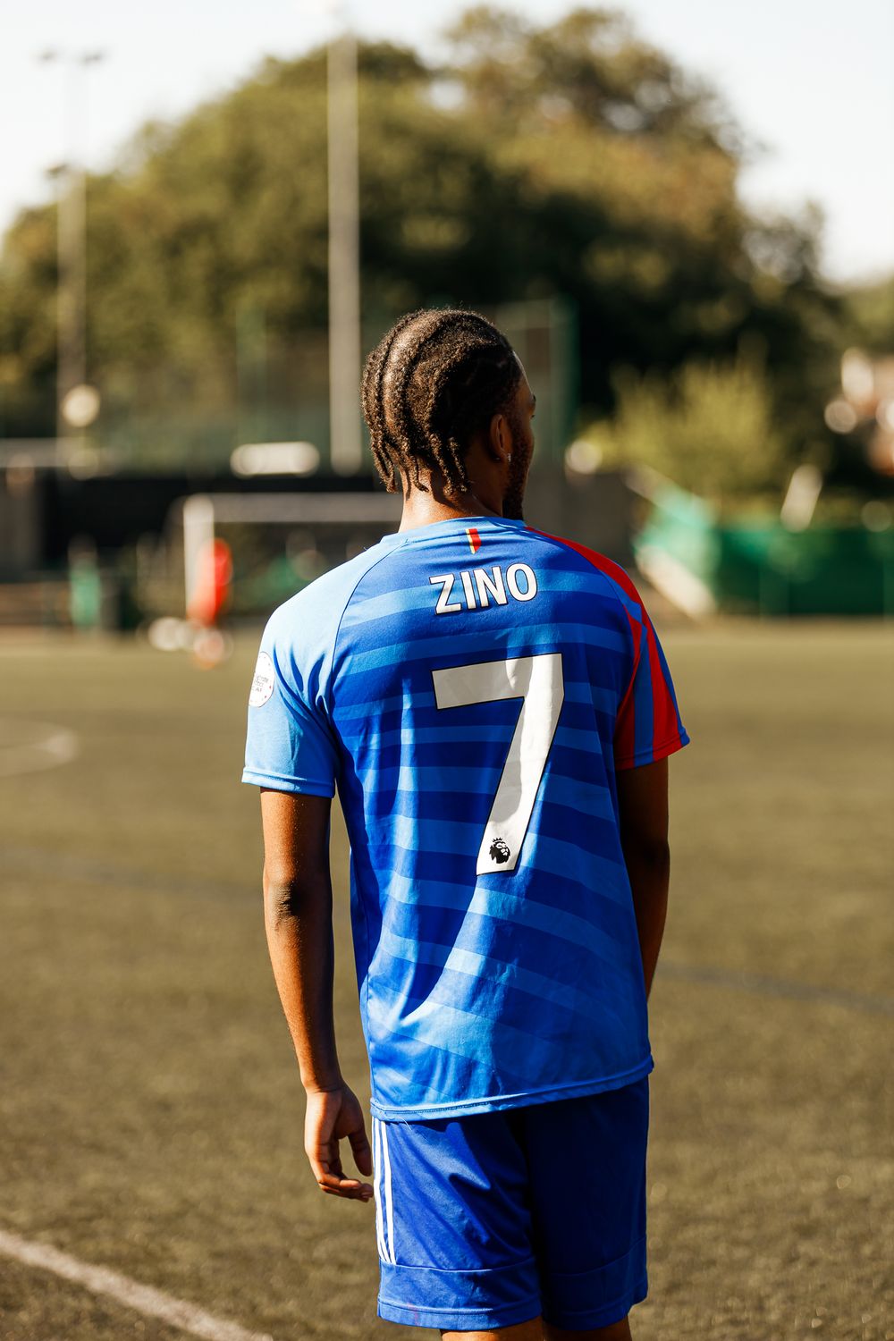 Soccer player wearing blue jersey with number 7 stands on field during golden hour lighting.