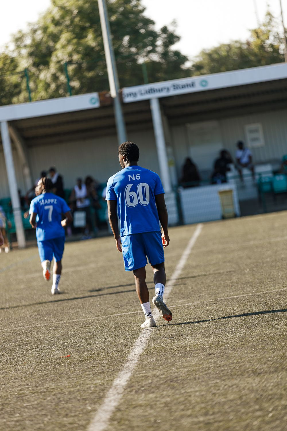 Soccer players in blue jerseys run across a grass field during an outdoor match.