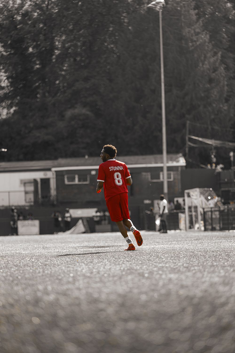 A baseball player in a red uniform walks alone across a snowy field on a winter day.