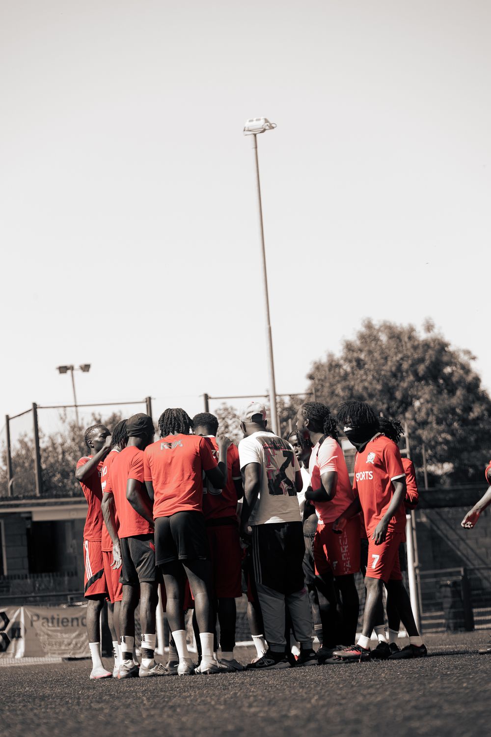 A group of athletes in red jerseys huddle together on a sports field during practice or a game.