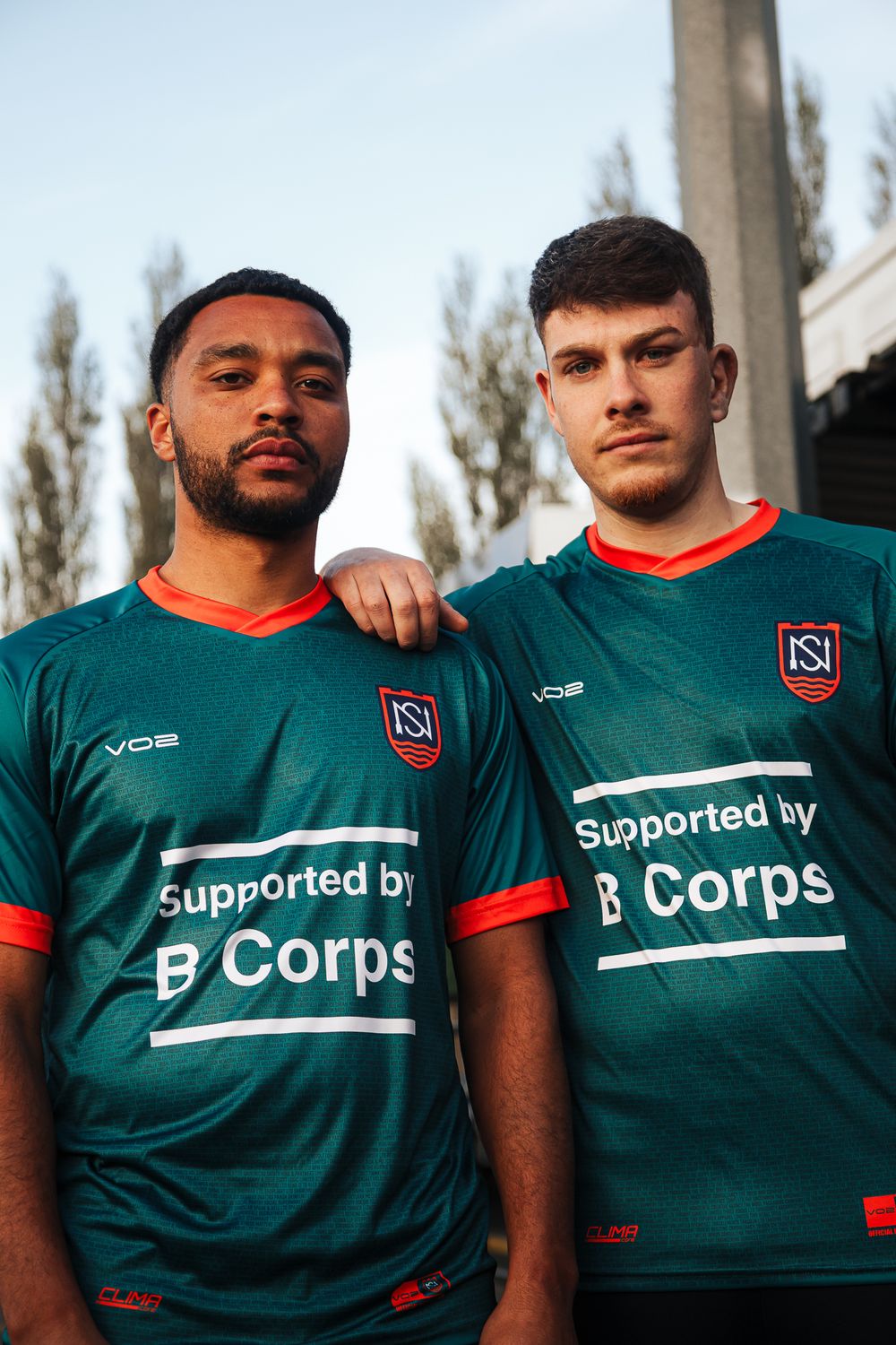 Soccer team players wearing dark teal jerseys with B Corps sponsorship stand together for a team photo.