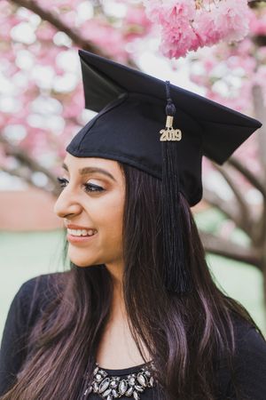 Close up view of graduate with class of 2019 cap posing under pink cherry blossoms.