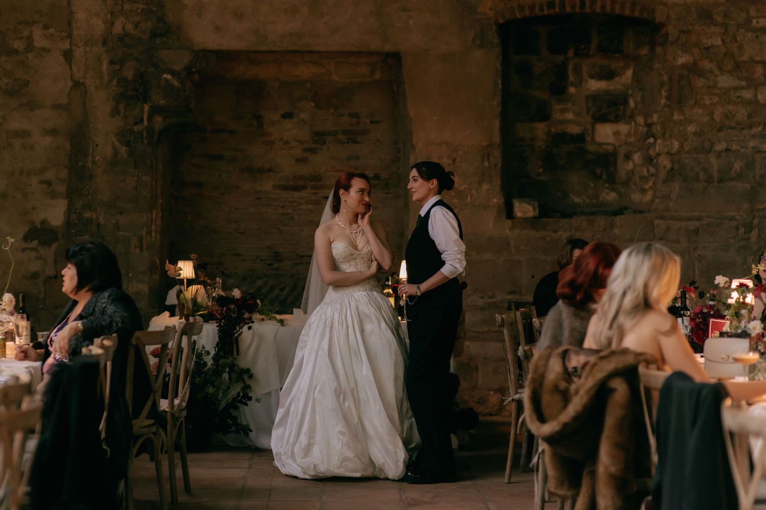 A couple shares their first dance at a rustic stone venue while guests look on during an intimate wedding reception.