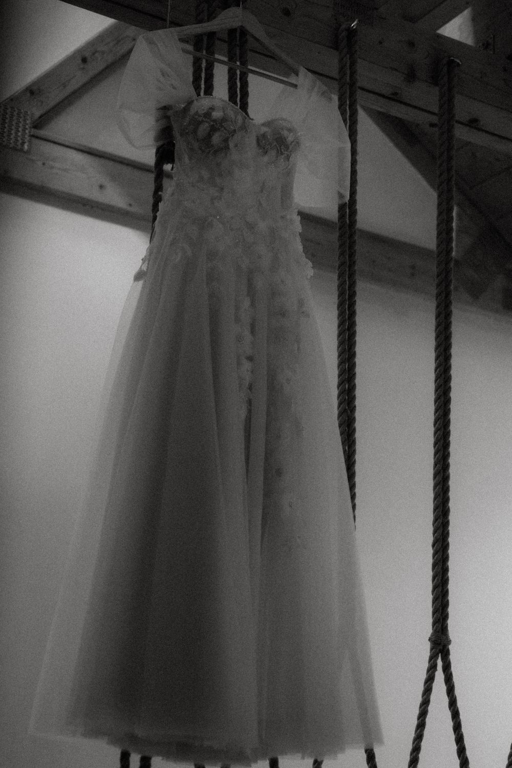 White tulle wedding dresses hanging from black ropes create an ethereal display in a dimly lit space.