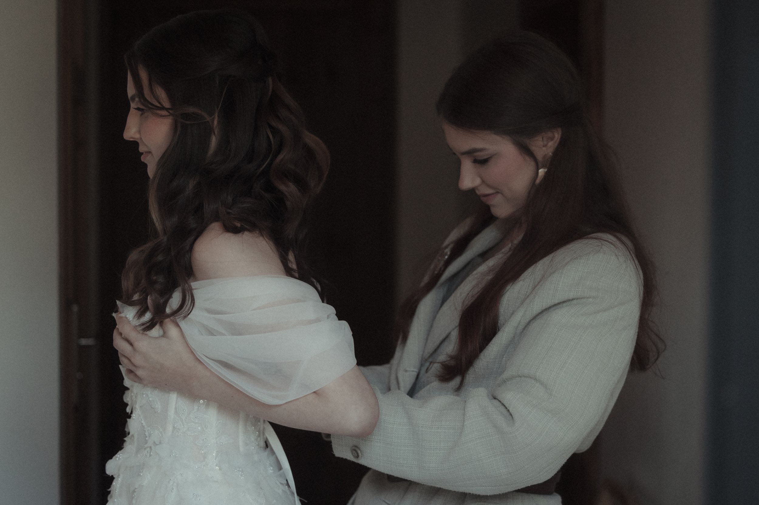 A couple embraces in a romantic moment wearing white outfits against a dark background.